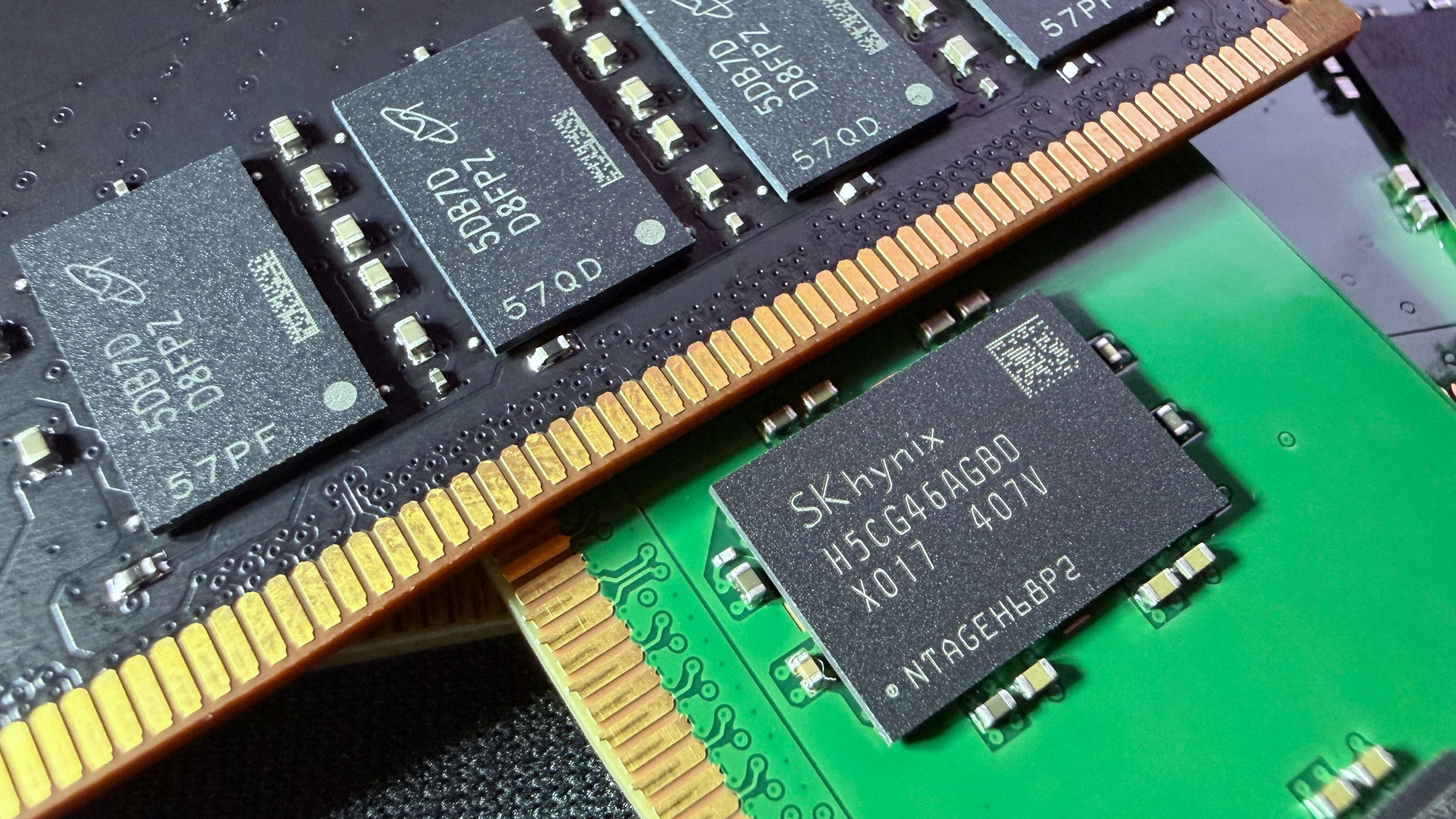 A close-up photo of a pair of Micron and SK Hynix DDR5 DIMMs, showing the memory modules on black/green PCBs