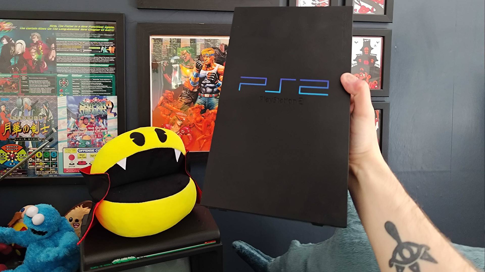Phil holding an original PS2 with one hand next to vampire Pac-Man plush.
